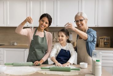 Little girl baking pie playing with young mom elderly...