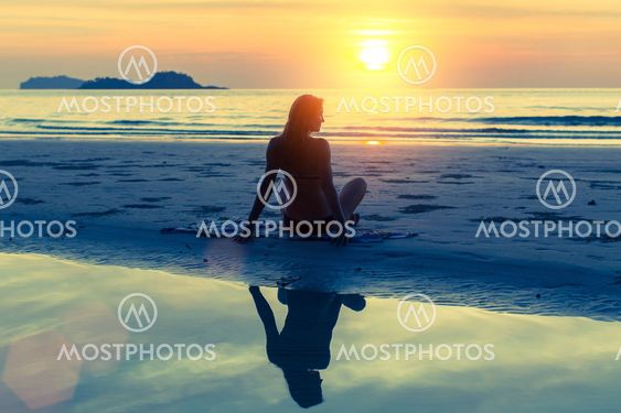 Silhouette of young beautiful girl sitting on the beach during sunset.