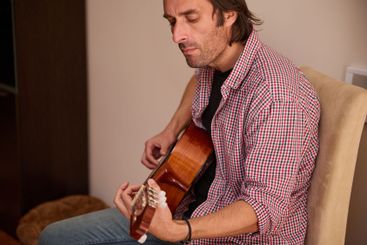 Man playing an acoustic guitar while seated indoors in a...