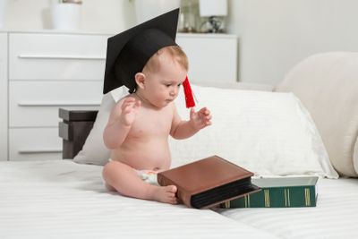 Naked baby boy wearing black graduation cap looking at...