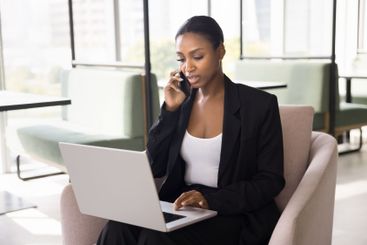 Businesswoman talk on smartphone using laptop seated in...