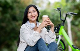 A smiling asian woman is holding a cup with both hand...