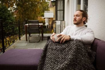 Young man with coffee cup and blanket sitting on patio