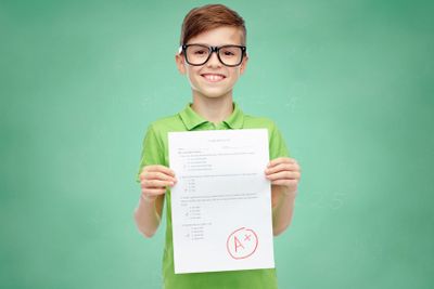 happy boy in eyeglasses holding school test result