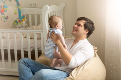 Portrait of young man playing with his baby at bedroom