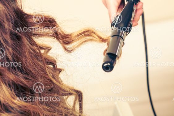 Stylist curling hair for young woman.
