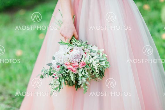 Bride in tender rose dress is holding stylish bouquet.