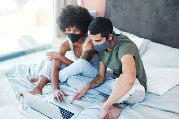 Couple, mask and laptop on bed in home with quarantine...