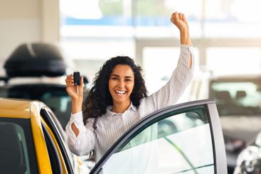 Emotional brunette woman buying new car, showroom interior