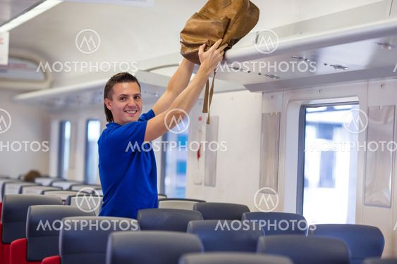 Young caucasian man putting luggage on the top shelf at...