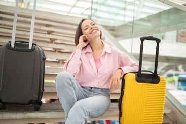 Cheerful traveler sitting on stairs beside luggage at an...