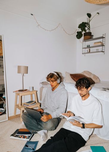 Young male roommates studying together while sitting by...