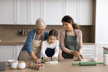 Older grandma young mum little girl cook pie at kitchen