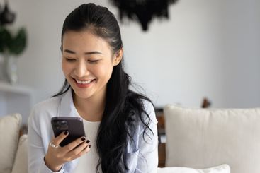 Happy beautiful young Asian woman chatting on cell phone