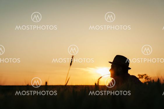 Young man resting in the wheat field at the sunset