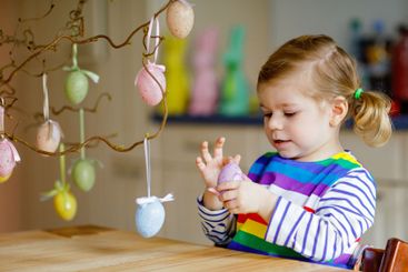 Cute little toddler girl decorating tree bough with...