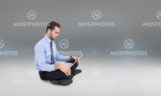 Composite image of cheerful businessman sitting on the floor using laptop