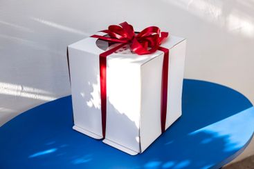 A white cardboard holiday box with a red silk bow....
