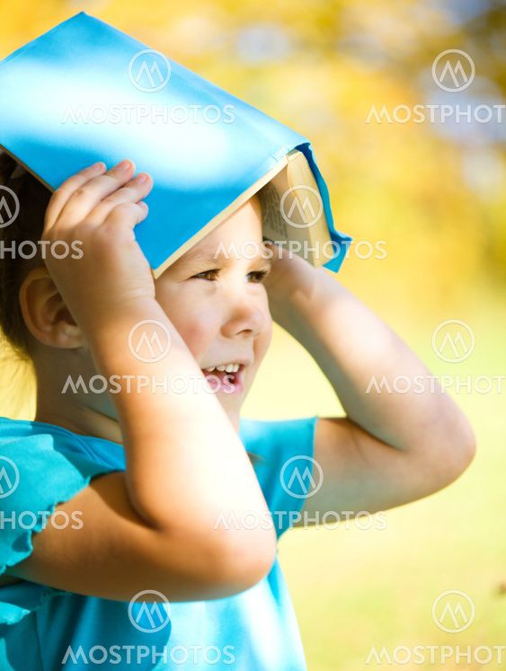 Little girl is playing with book outdoors
