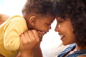 Close Up Of Mother And Baby Daughter Cuddling On Sofa At...