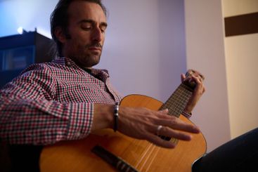 Man strumming an acoustic guitar in a relaxed indoor...