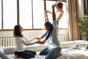 Playful biracial parents play with little daughter at home