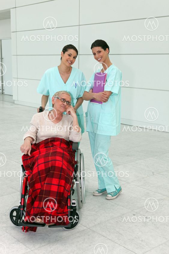Cheerful nurses with senior woman in wheelchair