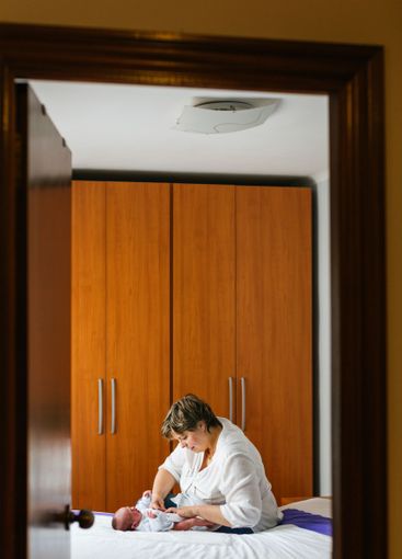 Mother changing diaper of one month old baby son on bed