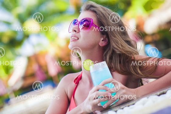 Beautiful woman with tropical cocktail in the pool