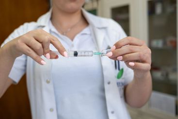 A focused nurse in a white lab coat carefully prepares a...
