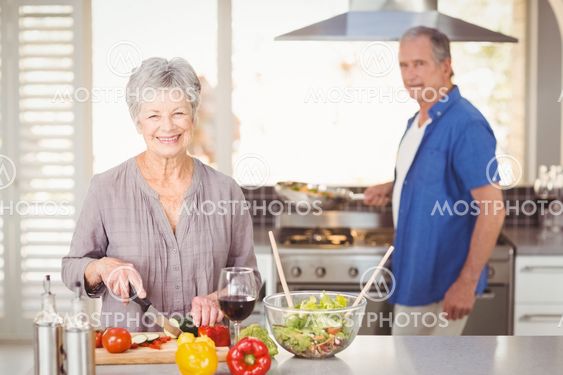 Happy senior woman cutting vegetables with husband in...