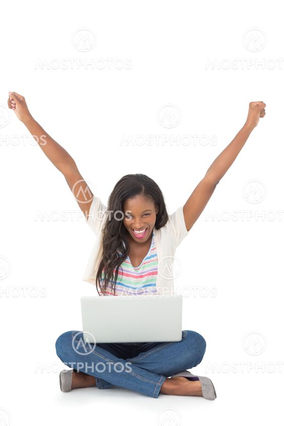 Pretty young woman cheering at camera with laptop sitting on floor