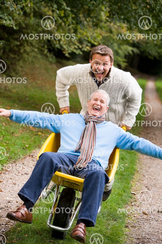 Grown up son pushing father in wheelbarrow