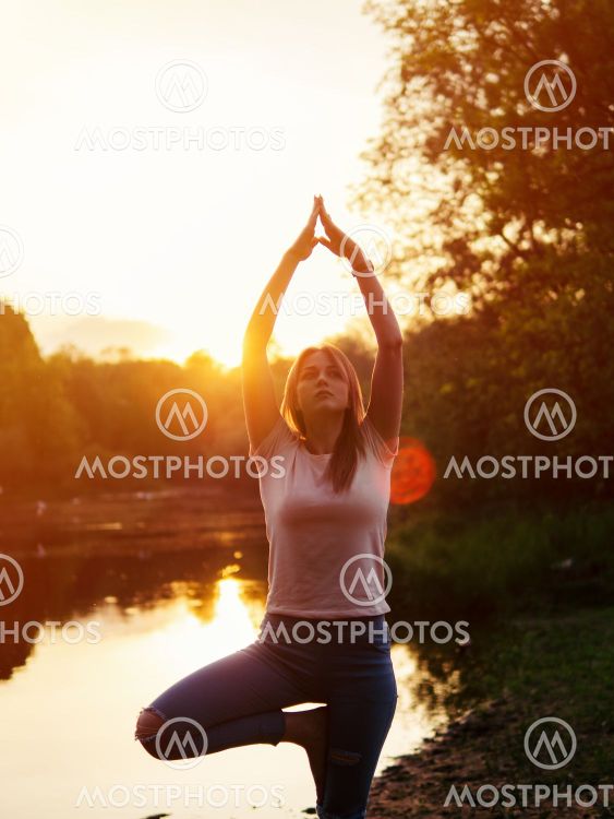 Beautiful Caucasian young woman doing yoga on the river...