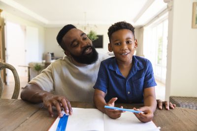 Happy african american father and son sitting at table...