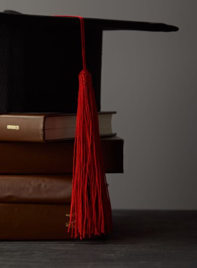 Brown books and academic cap with red tassel isolated on...