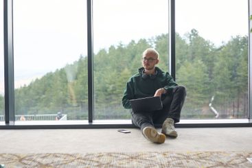A blonde man sitting on the floor of a modern office,...