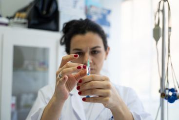 A focused nurse in a white lab coat carefully prepares a...