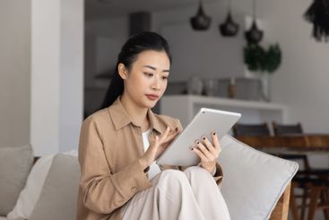 Focused young Asian woman using digital online...