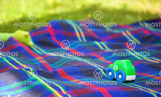Summer picnic with a child. Small toy car on a checkered blanket laid on the grass for children's games