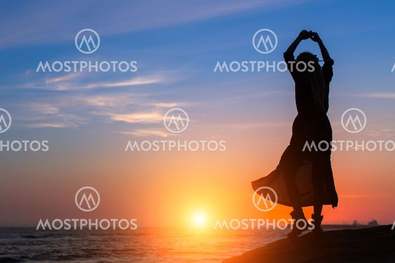 Silhouette of dancing woman on the sea coast during amazing sunset.