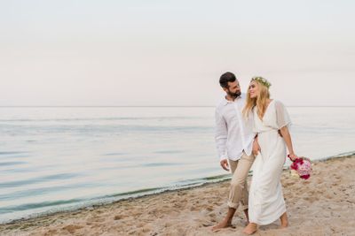 smiling bride and groom hugging and walking on seashore