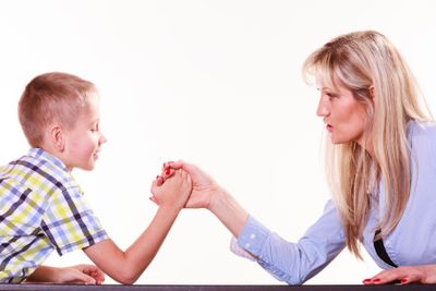 Mother and son arm wrestle sit at table.