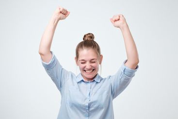 young female winner raising arms exclaiming with joy and...