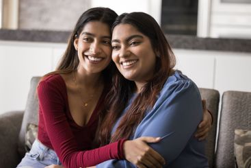 Two sisters sit close together on sofa in living room