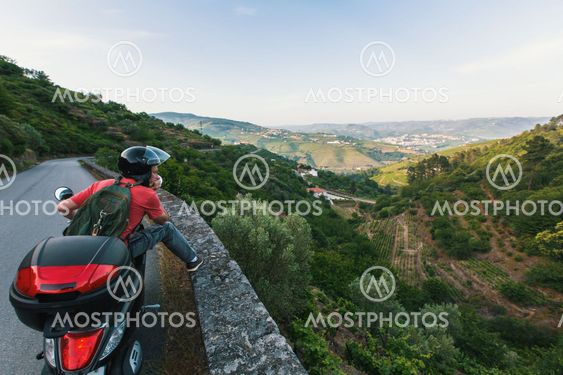 Young man travels on a motorcycle stopped at a view point and looking at the Douro Valley, Portugal.