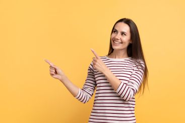 Positive young brunette woman pointing at copy space