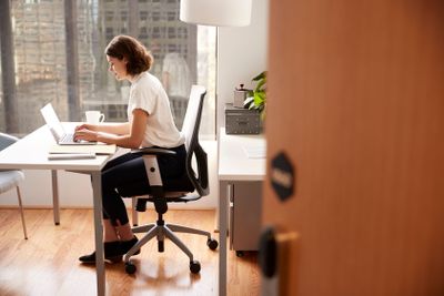 Businesswoman Sitting At Desk Working On Laptop In Modern...
