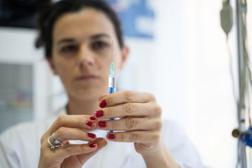 A focused nurse in a white lab coat carefully prepares a...