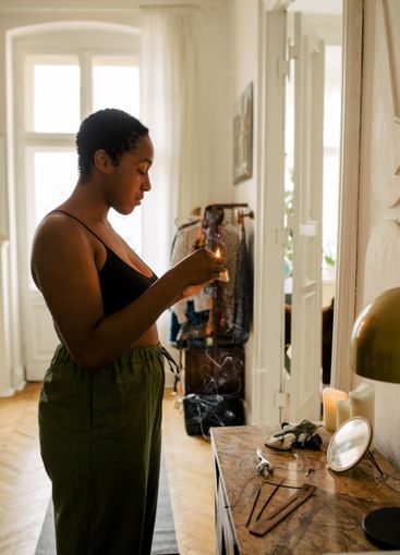 Side view of young woman holding lit candle at apartment